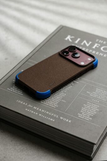 A brown textured phone case with blue corners resting on a grey hardcover book